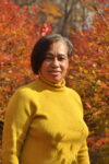 woman in yellow turtleneck shirt standing in front of trees with orange leaves